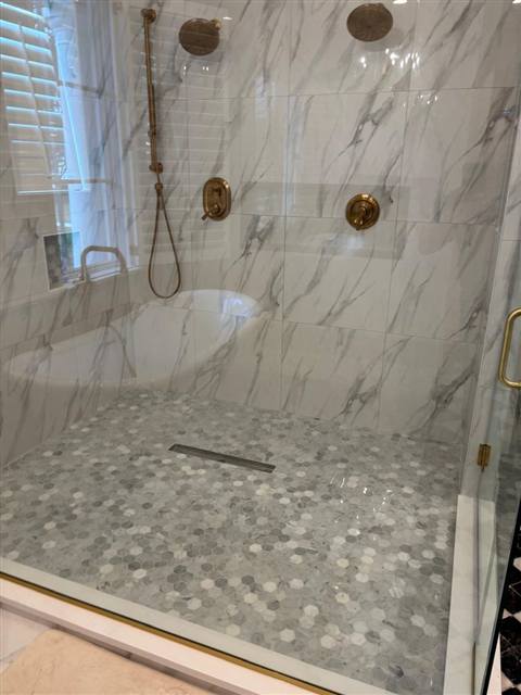 Ducha con grifería dorada y piso de mármol hexagonal