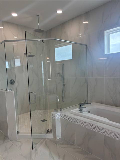 Ducha de vidrio sin marco y bañera revestida de azulejo